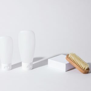 Clean minimalist photo of skincare bottles with a wooden brush on a white background.